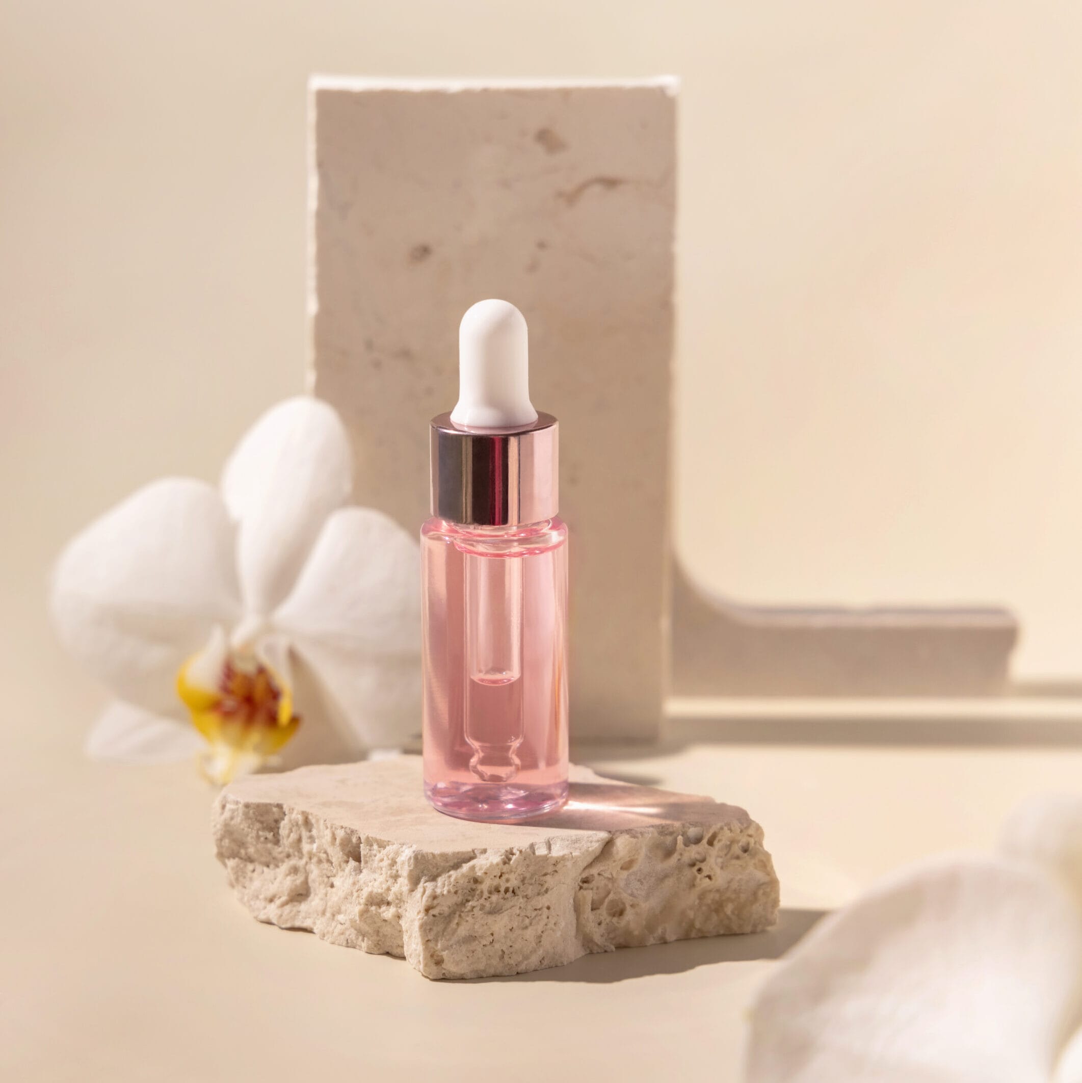 Dropper Bottle on stone near white orchid flowers on light yello