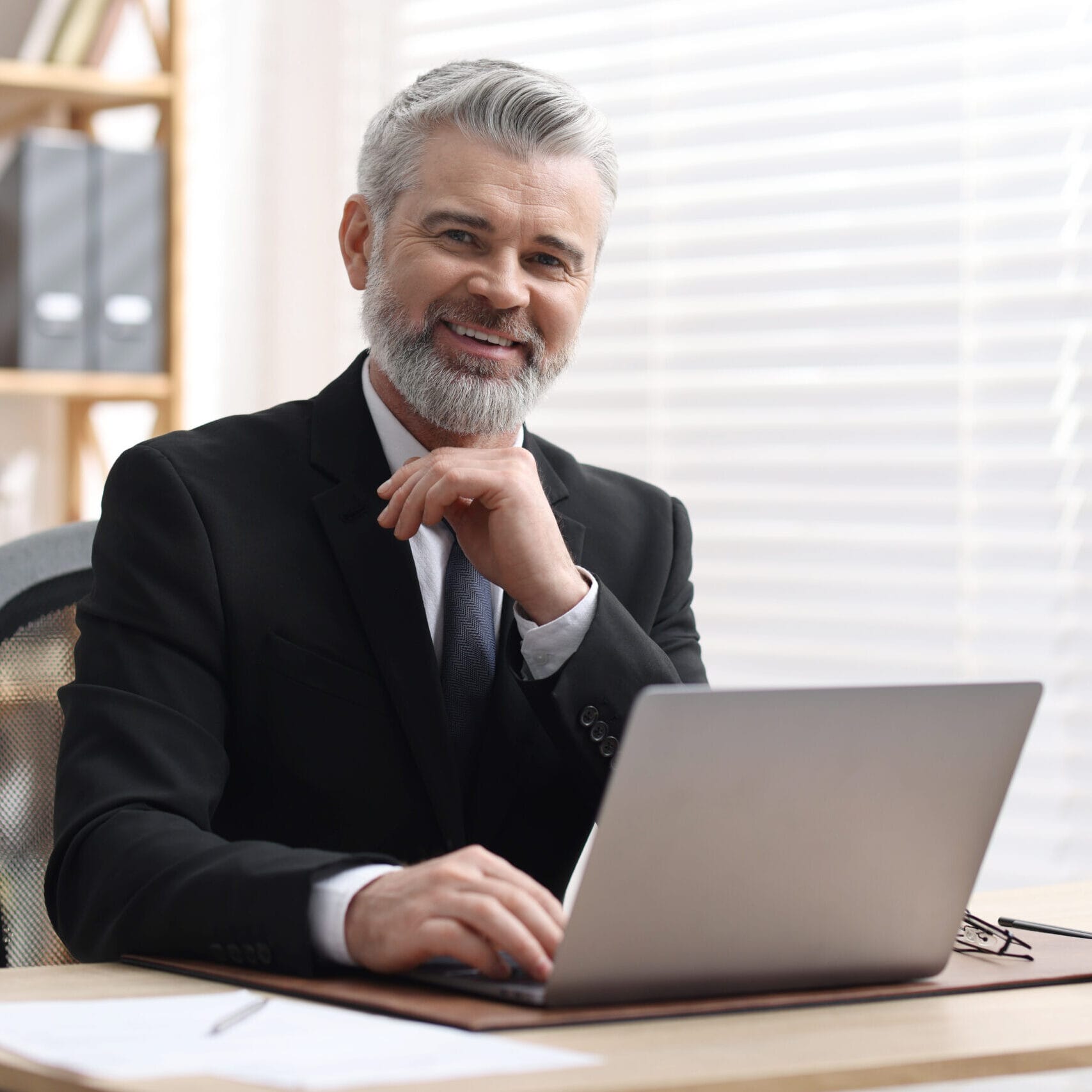 Portrait of smiling notary in suit with laptop at table in offic siti per avvocati