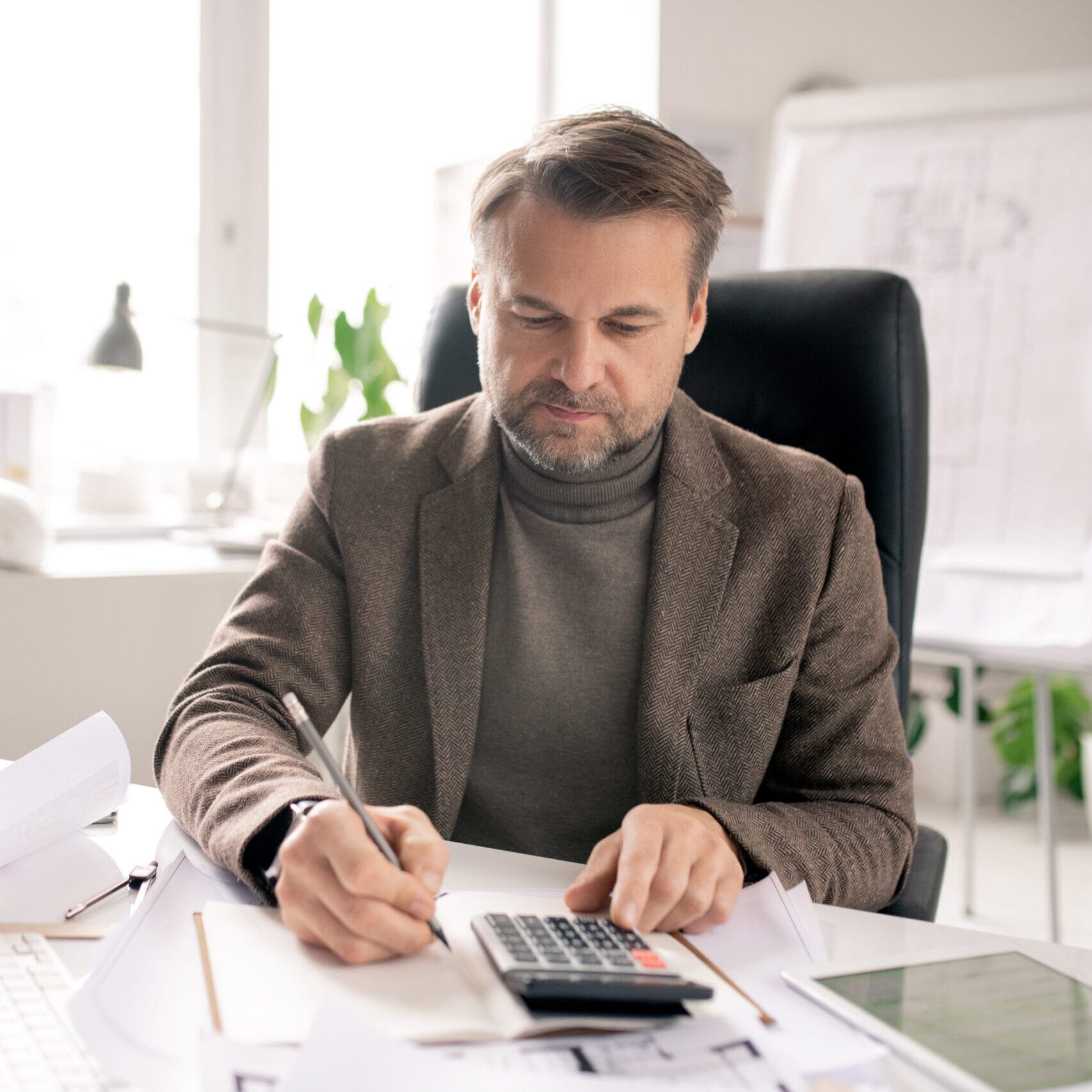 Mature engineer or accountant with pen and calculator making notes in notebook siti per commercialisti