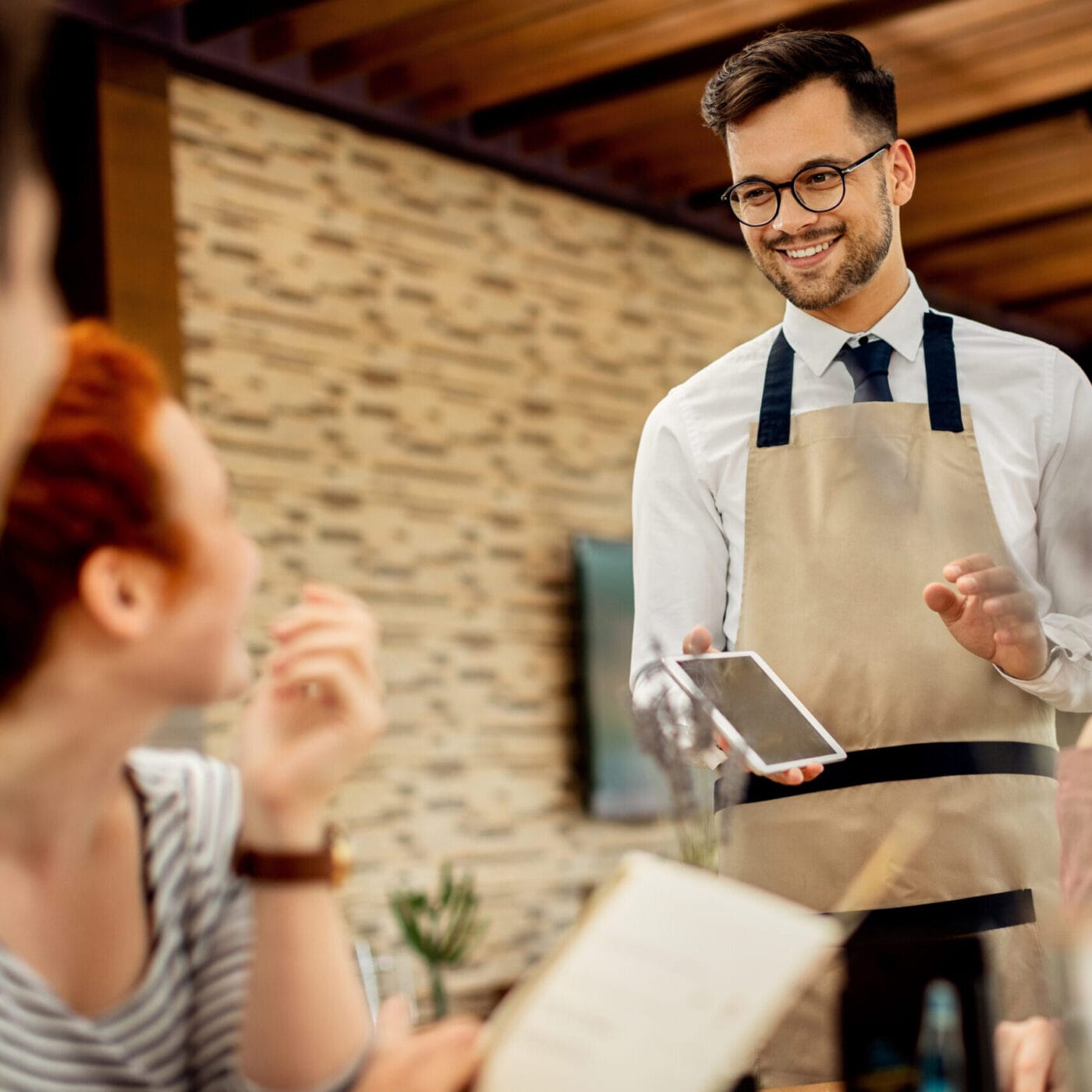 Young happy waiter taking order from his guests in a cafe. menu digitale per ristoranti